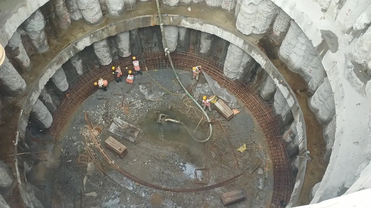 Top-down view into a circular shaft ringed by bored piles, with crew fixing reinforcement at the base