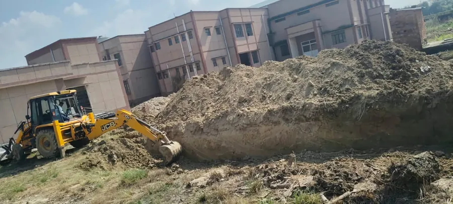 Backhoe excavating beside existing school blocks at Pratappur Chamurkha